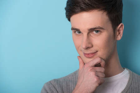 Thoughtful young men looking at camera and holding his hand on chin. young casual man standing on blue background and smilingの写真素材