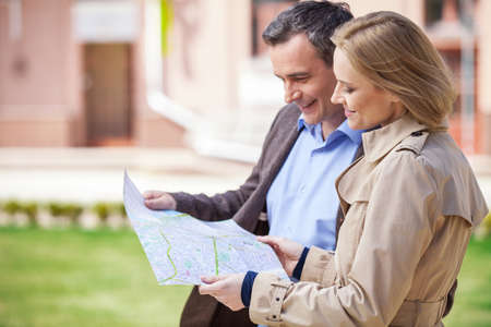 beautiful elegant mid age couple standing outdoors. side view of smiling woman holding map and looking at mapの写真素材