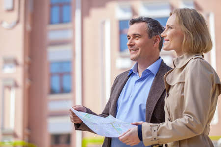 beautiful elegant mid age couple standing outdoors. side view of smiling woman holding map and looking aheadの写真素材