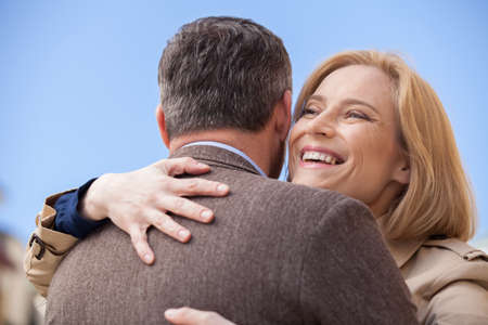 back view of man hugging happy woman outside. Smiling blond woman embracing man outsideの写真素材