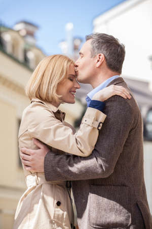 side view of man hugging happy woman outside. Smiling blond woman embracing man outsideの写真素材