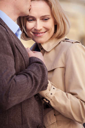adult couple standing on street and hugging. happy man kissing smiling woman on foreheadの写真素材