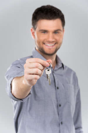 Businessman holding key with focus on key. Holding out keys and smiling on grey backgroundの写真素材
