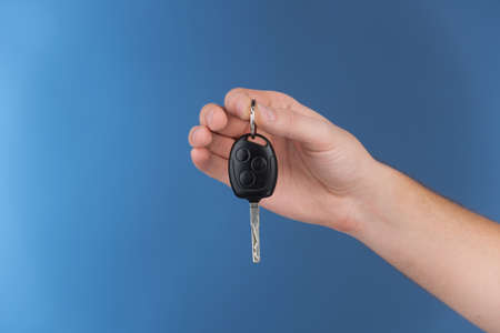 hand holding key on blue background. male hands with keys hanging in air with black plastic