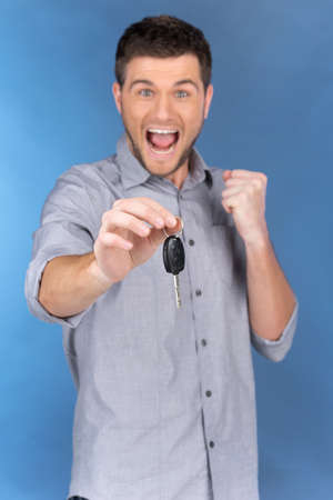 Happy man holding car keys on blue background. Casual young man holding ignition keys and smilingの写真素材