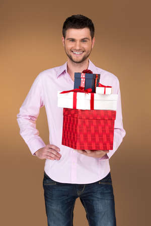 close-up on smiling guy holding many boxes. waist up of happy male carrying pile of boxes on brown backgroundの写真素材
