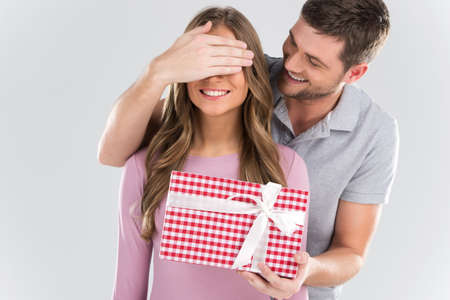 Man surprising his girlfriend with gift on grey background. man covering eyes of girl and standing behindの写真素材