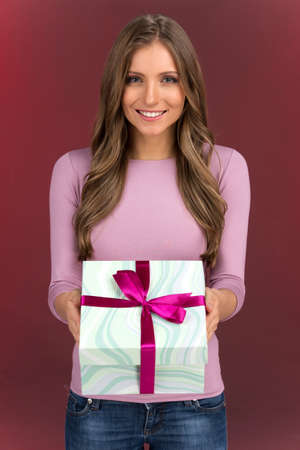 Gorgeous cute young woman holding present box. brunette girl holding present and looking into cameraの写真素材
