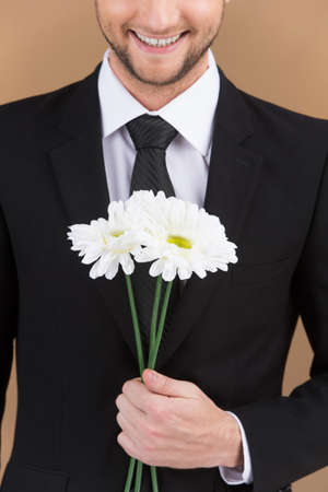 white flowers in hands of smiling man. closeup on guy wearing black suit holding flowersの写真素材