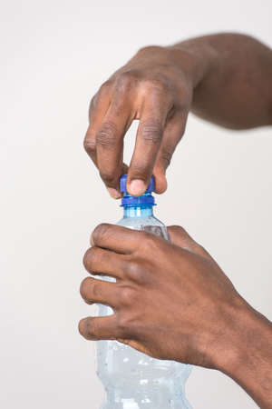 man hand with bottle of water isolated on white background. african black man opening bottle of still waterの写真素材