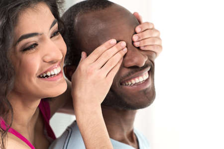 young girl covering her boyfriend eyes with both hands. Young woman covering african black man eyesの写真素材