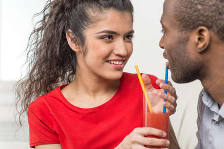 Young couple sharing glass of orange juice. black man and indian woman drinking juiceの写真素材