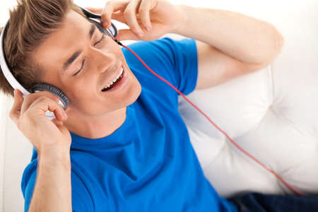 Happy man in headphones relaxing on sofa at home. の写真素材