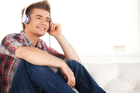 Happy man in headphones relaxing on sofa at home. の写真素材