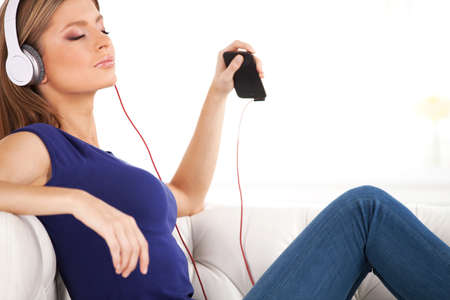 beautiful young girl listens to music on headphones. Happy woman with headphones resting on sofaの写真素材