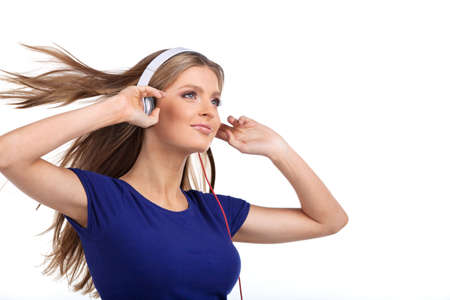 Cheerful young woman listening music with headphones. side view of pretty brunette standing on white background and holding headphonesの写真素材