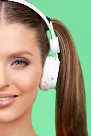 Half face of pretty young girl listening music. girl standing isolated on green backgroundの写真素材