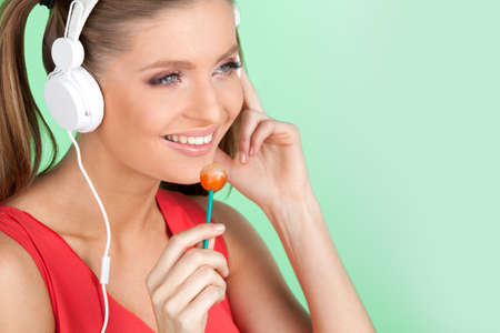 funny colorful girl listening music on green background. Sexy woman listening to music on headphones and licking lollipopの写真素材