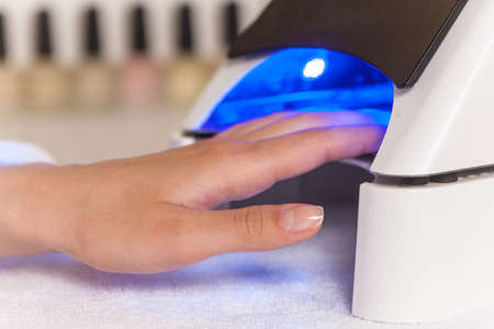 Manicure in process using Uv lamp for nails. client woman drying nails at manicurist salonの写真素材