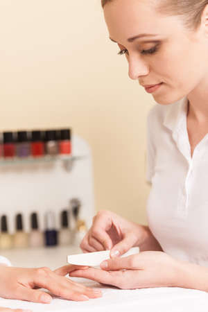 Close-up Of Beautician Hand Filing Nails Of Woman In Salon. manucurist women sitting in spa salon and looking at fingersの写真素材