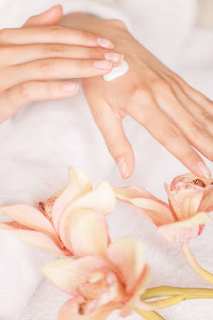 closeup of woman hands with white cream. image of beautiful female hands and fingers with flowers and towelの写真素材