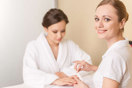 Close-up of beautician hand filing nails of woman in salon. manucurist women sitting in spa salon and looking at cameraの写真素材