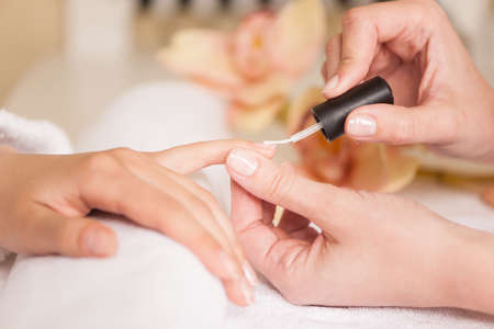 Woman in nail salon receiving manicure by beautician. closeup of female hand resting on white towelの写真素材