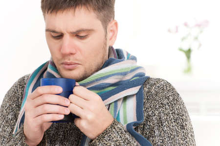 closeup on man on sofa drinking hot tea. young man holding cup on sofa in living roomの写真素材