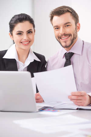 Cheerful business people sitting at table with laptop. Young colleagues sitting in elegant office, working on laptop, smiling.の写真素材