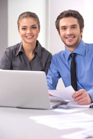Cheerful business people sitting at table with laptop. Young colleagues sitting in elegant office, working on laptop, smiling.の写真素材