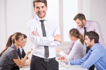 Business meeting - manager discussing work with his colleagues. man standing on foreground with crossed hands and team on backgroundの写真素材
