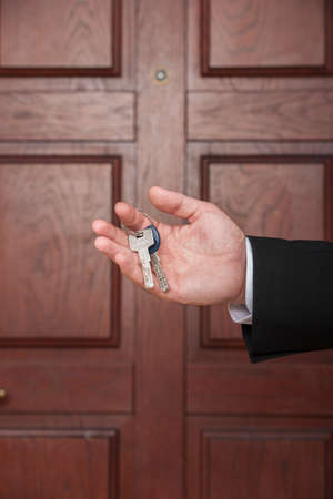 closeup on man hand holding keys to apartment door. real estate agent with keys on brown doorの写真素材