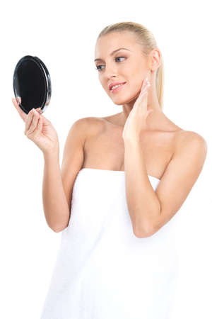 Portrait of beautiful woman looking at mirror. attractive blond looking at mirror in bright studio and using creamの写真素材