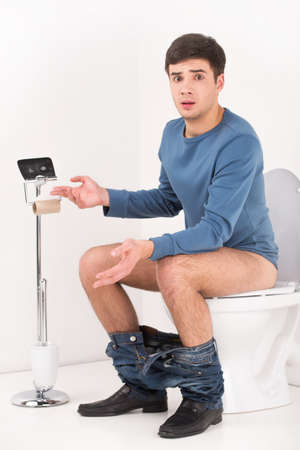 Young handsome man sitting on toilet. guy without toilet paper upset and made helpless gestureの写真素材