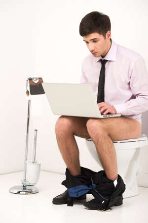 Man with laptop computer sitting on toilet. Businessman typing letter on notebook while sitting on toiletの写真素材