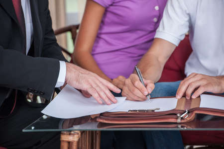 closeup on happy man hand signing agreement on new house. agent giving documents to young couple purchasing new houseの写真素材