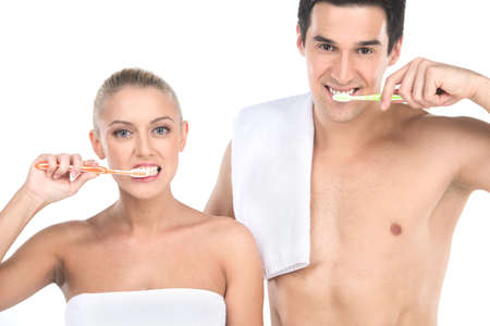 Close up of sexy fit man and woman brushing teeth with toothbrushes. Standing couple isolated over white background looking into cameraの写真素材