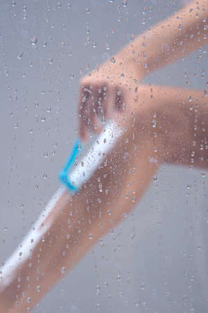 Beautiful girl shaving her legs with razor. picture of girl shaving leg trough transparent glassの写真素材