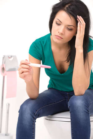 closeup on woman holding pregnancy test with two stripes. Worried girl looking at pregnancy test in bathroomの写真素材