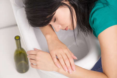 Young caucasian woman in toilet - drunk concept. Young dark-haired woman vomiting in toiletの写真素材