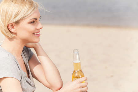 Woman sitting on beach and drinking beer. summer holidays and vacation spent on lake shoreの写真素材