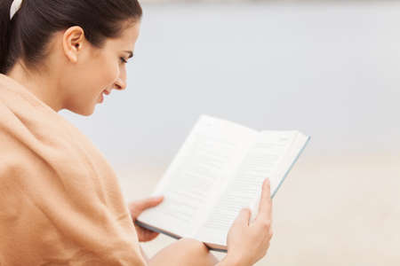 over shoulder view of woman reading book covered with blanket. の写真素材