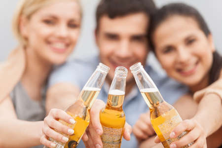 Man and two women relaxing on beach with beer. の写真素材