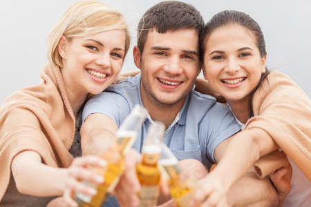 Man and two women relaxing on beach with beer. の写真素材