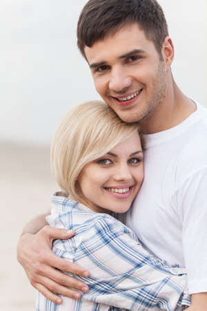 Attractive young couple standing on beach at summer. happy woman and man standing hugging and smilingの写真素材
