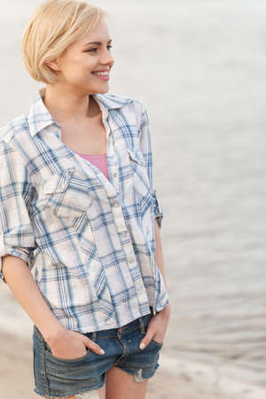 Young woman in shirt and jeans standing on sea shore. の写真素材