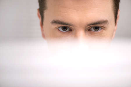 handsome technical support operator working on computer. male eyes behind computer at bright center...
