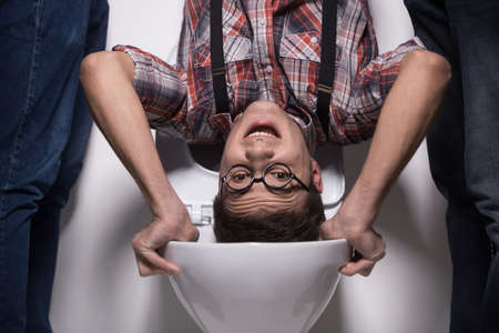 man is standing upside down on toilet bowl. closeup on two man holding man over toilet seatの写真素材