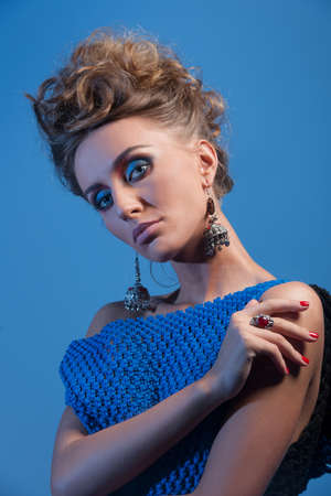 beautiful blonde woman wearing blue dress and jewelry. closeup on pretty girl looking into camera on blue backgroundの写真素材