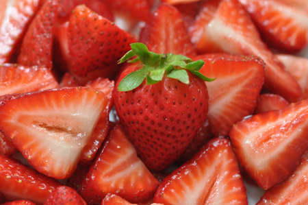 A single fresh strawberry on a bed of juicy strawberry slicesの写真素材